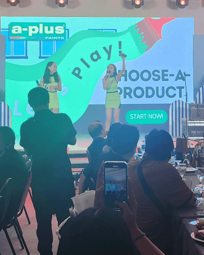 Hosts energize the crowd with engaging prize announcements and fun giveaways. Two women on stage hosting a prize giveaway, engaging the audience with smiles and excitement