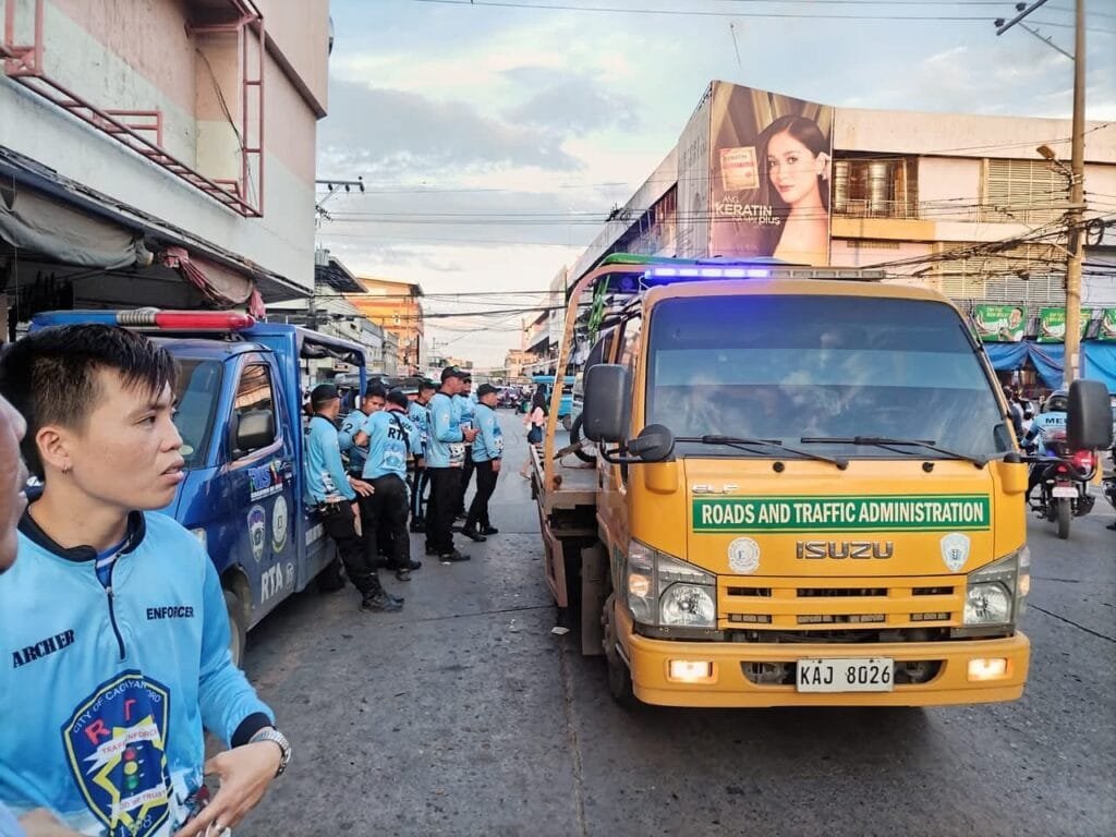 Rta traffic enforcement cagayan de oro personnel in blue uniforms standing near a yellow isuzu rta truck with 'roads and traffic administration' signage in a busy street of cagayan de oro city.