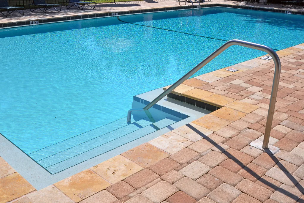 Swimming pool services (1024 x 683 px) A sparkling swimming pool with clean, clear water, brick paver surroundings, and a stainless steel handrail, showcasing premium pool design and functionality.