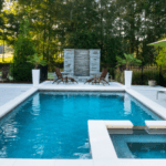A beautifully designed outdoor swimming pool with crystal-clear water, a jacuzzi, and a modern stone feature wall, surrounded by lush greenery and lounge chairs.