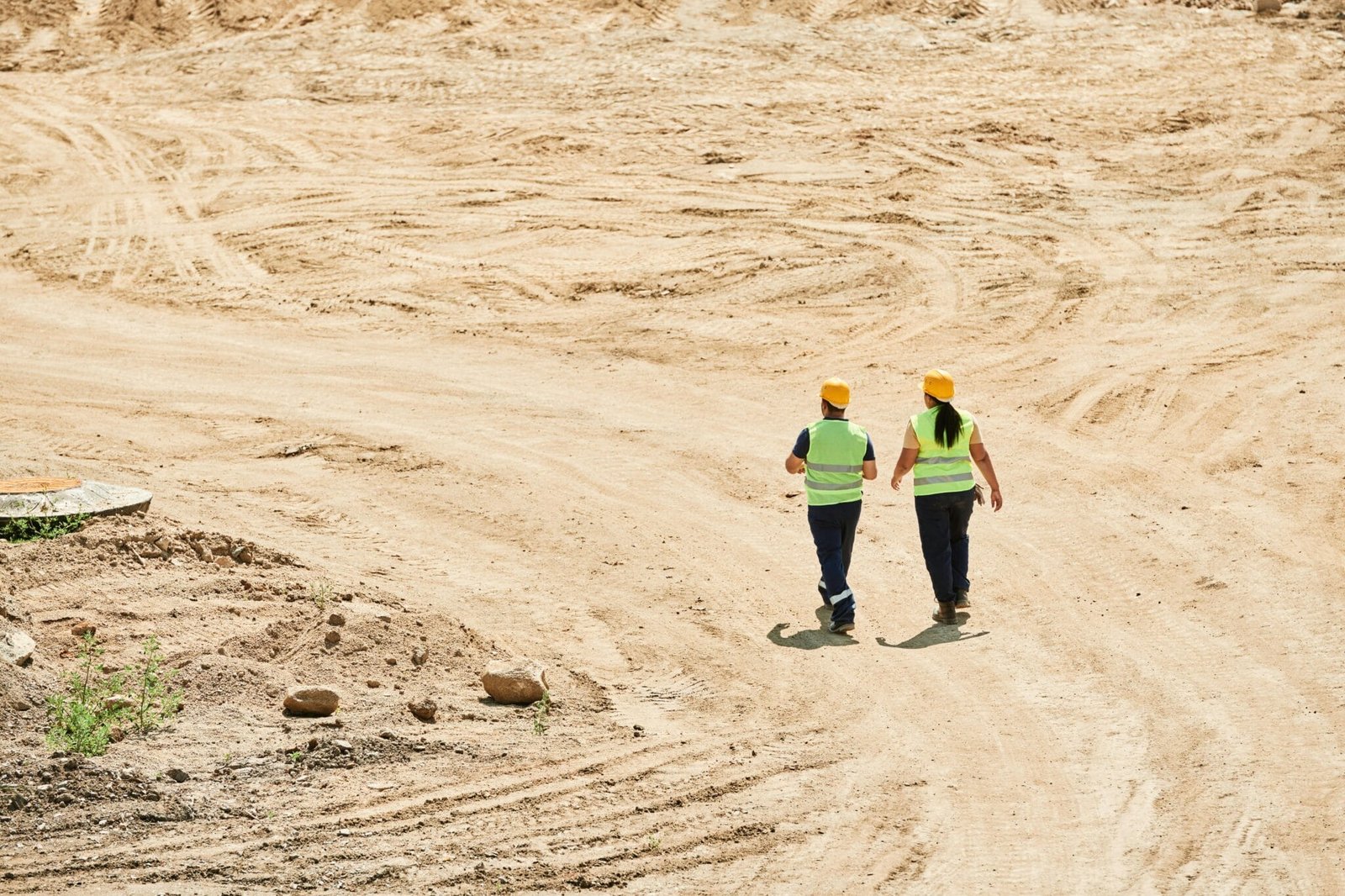 Two construction management workers in safety gear walk through a dusty construction site, highlighting teamwork and industry.