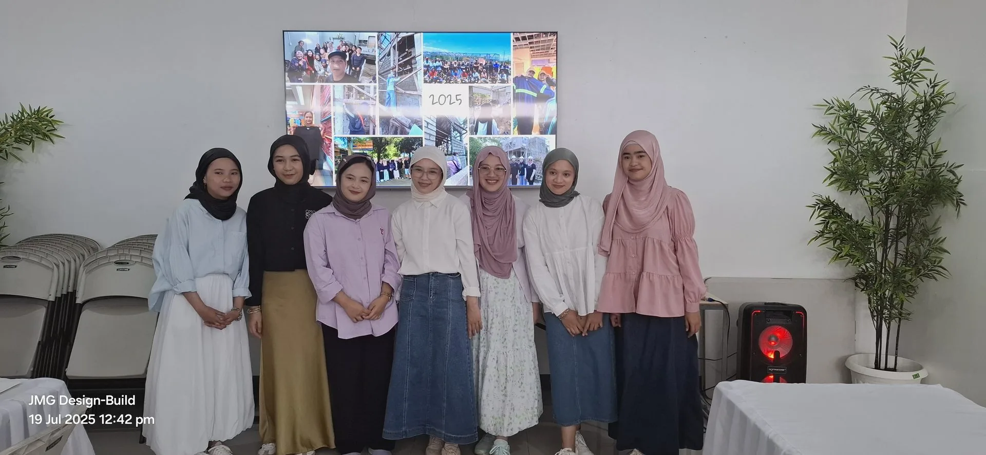 Jmg staff and interns posing together outside the company office beneath the jmg construction & general merchandise signboard
