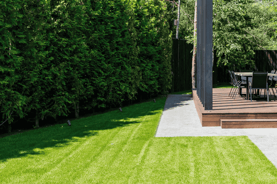 🌿 exterior & landscaping A neatly landscaped backyard with trimmed grass, elevated wooden deck, and patio chairs surrounded by greenery.