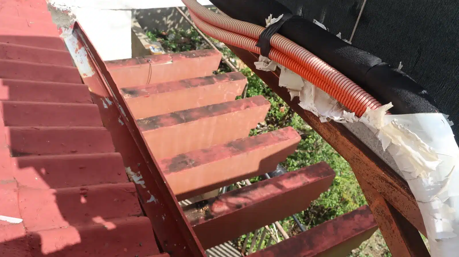Property condition assessment & indicative value range: camella gran europa, lumbia, cagayan de oro 16 Red-painted exterior stair with peeling paint and a rusting steel stringer beside a taped conduit, camella gran europa house, cagayan de oro