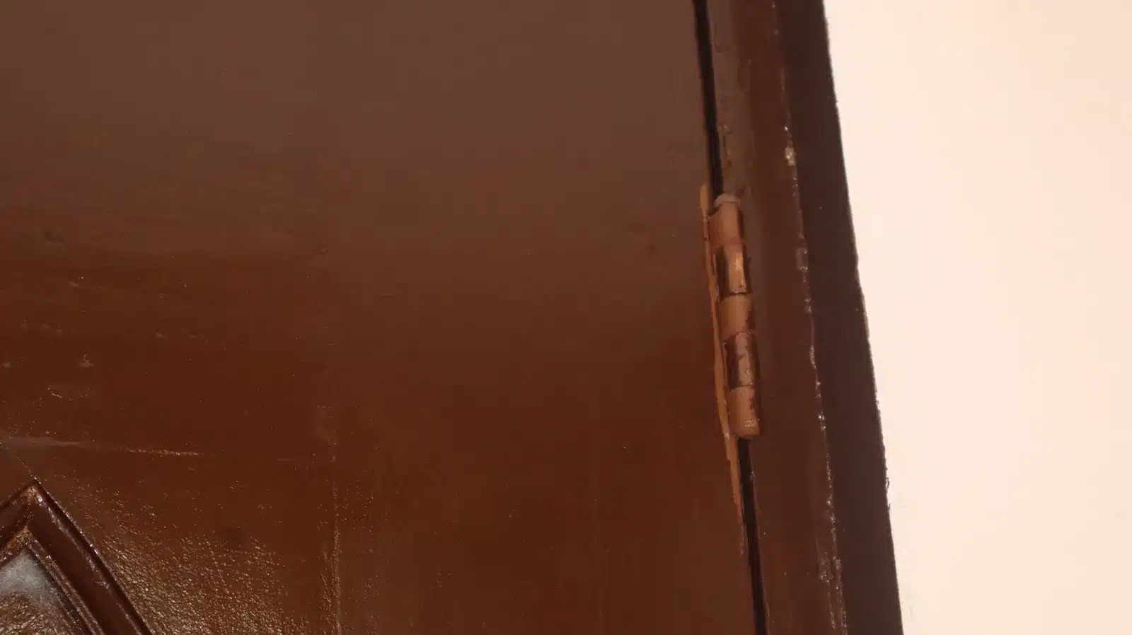 Property condition assessment & indicative value range: camella gran europa, lumbia, cagayan de oro 22 Close-up of a door hinge and brown-painted door edge beside a cream wall, camella gran europa house, cagayan de oro